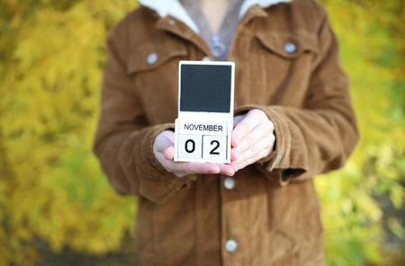 Woman holding calendar with date November 02 on yellow autumn leaves backgroundの写真素材