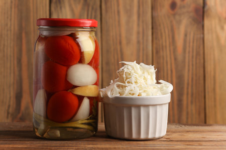 Sauerkraut in a ceramic bowl and tomato and Pickled Canned tomatoes in glass jars on wooden backgroundの写真素材