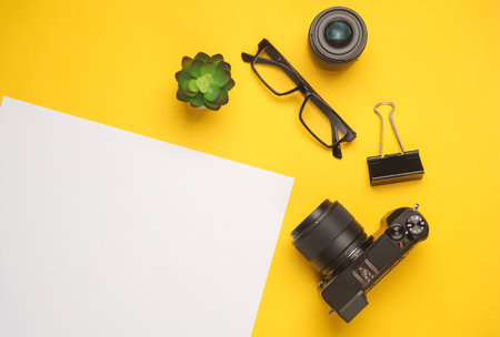 Camera and accessories with white blank sheet of paper for text on yellow background