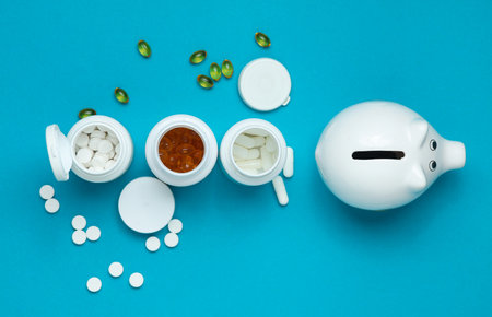 Different Pills in plastic bottles and piggy bank on blue background. Medicine concept. Top viewの写真素材