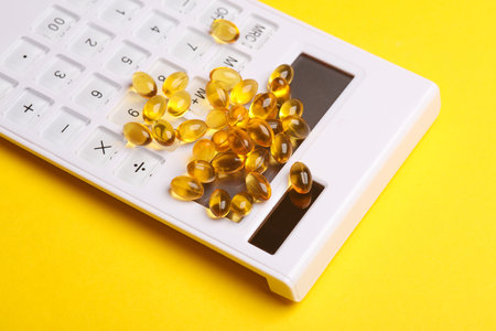Fish oil capsules and calculator on yellow background.の写真素材
