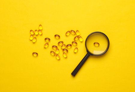 Fish oil capsules with magnifying glass on yellow backgroundの写真素材