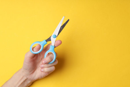 Hand holding scissors for creativity on a yellow background