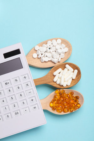 Pills in wooden spoons and calculator on blue backgroundの写真素材