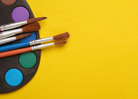 Watercolor paint palette with brushes on a yellow backgroundの写真素材