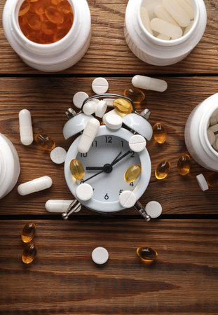 Different types of pills in white plastic bottles with alarm clock on a wooden table. Top viewの写真素材
