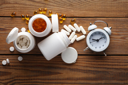 Different types of pills in white plastic bottles with alarm clock on a wooden table. Top viewの写真素材