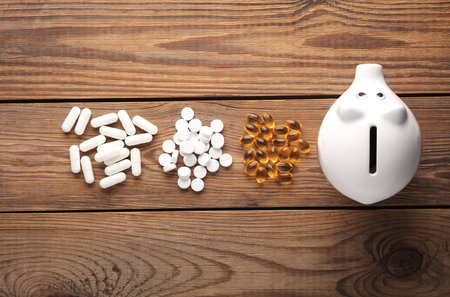 Piggy bank and different types of pills on a wooden tableの写真素材