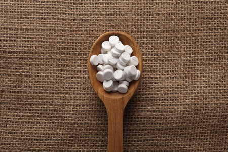 Pills in wooden spoon on burlap background