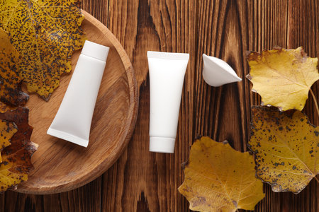 White cream tubes on a wooden plate with autumn leaves. Beauty mockupの写真素材