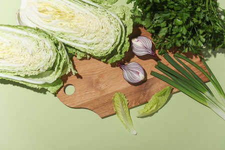 Fresh greenery, vegetables with kitchen board on a green background. Healthy food, vegetarians. Flat...