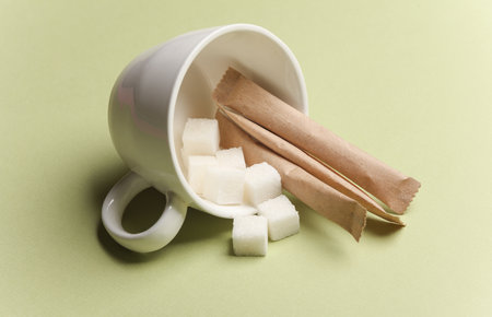 Ceramic cup with sugar cubes, disposable coffee packaging on green backgroundの写真素材
