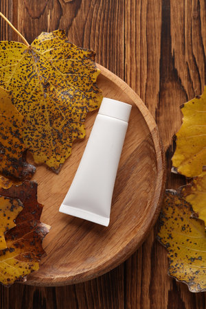 White cream tube on a wooden plate with autumn leaves. Beauty mockupの写真素材