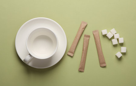 Ceramic cup with sugar cubes, disposable coffee packaging on green backgroundの写真素材
