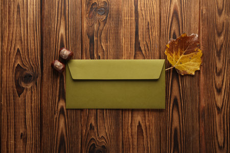 Autumn composition with an envelope, chestnut and yellowed leaf on a wooden background.