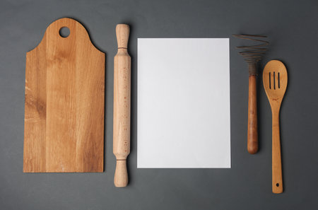 Set of wooden eco kitchen utensils and blank paper sheet on dark gray background. Flat lay. Top viewの写真素材