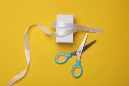 White box with satin ribbon and scissors on a yellow background. Holiday packagingの写真素材