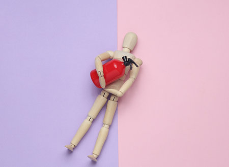 Wooden puppet holding Toy extinguisher on a pastel background. Top viewの写真素材