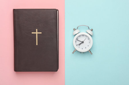 Bible book and alarm clock, wooden table. Prayer timeの写真素材