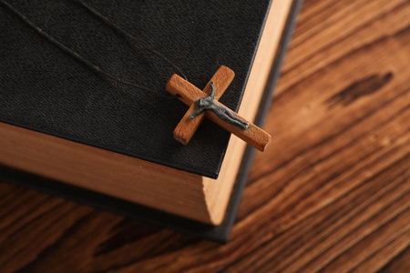 Bible book and wooden Christian cross on a string, wooden table