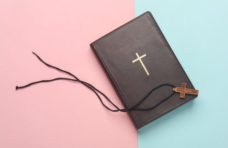 Bible book and wooden Christian cross on a string, pink blue background