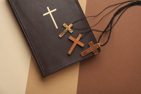 Bible book and wooden Christian crosses on a string, beige background. Top view