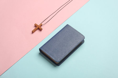 Bible book and wooden Christian cross on a string, pink blue background