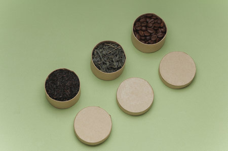 Green tea leaves and Coffee beans in cardboard round boxes on green backgroundの写真素材