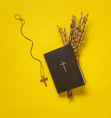 Willow twigs and Holy Bible book and cross on yellow background. Top view. Flat lay.の写真素材