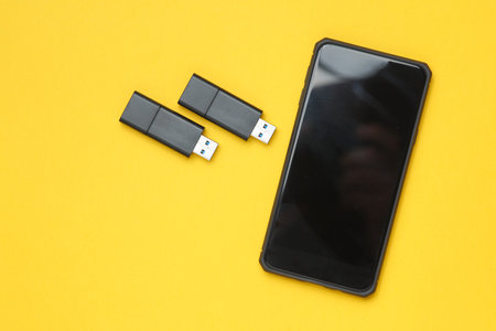 Smartphone and Two black USB flash drives on yellow background