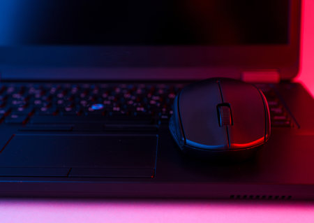 Modern laptop with pc mouse in blue-red gradient neon light