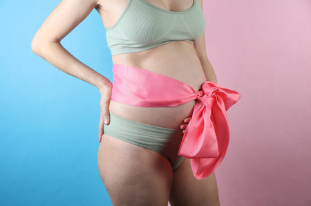 Pregnant woman in underwear with her belly tied in a bow on a blue-pink backgroundの写真素材