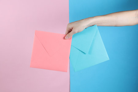 Female hand holding blue and pink envelopes on pastel backgroundの写真素材