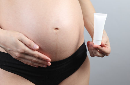 Pregnant woman in underwear holding cream tube on gray backgroundの写真素材