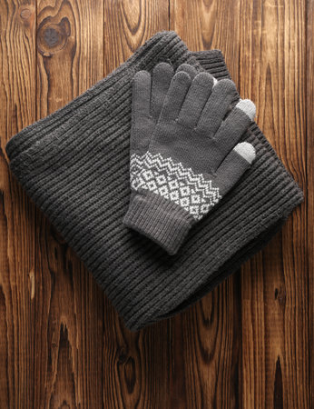 Knitted gloves and scarf on wooden background. Top view