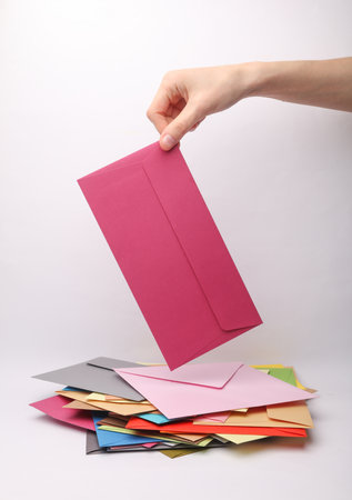 Hand holding a pink envelope among many colored envelopes on a white backgroundの写真素材