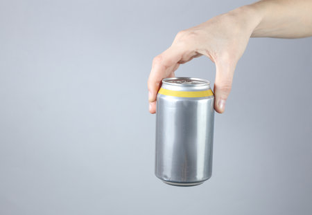 Hand holding Aluminum can for beer, soda or energy drink on gray studio background.