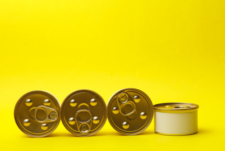 Tin cans of canned food with white labels on yellow background, mockup for your designの写真素材