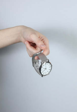 Female hand holding analog wristwatch on gray studio backgroundの写真素材