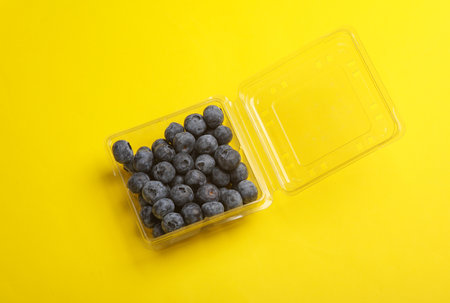 Blueberries in a transparent plastic box on a yellow background. Top viewの写真素材