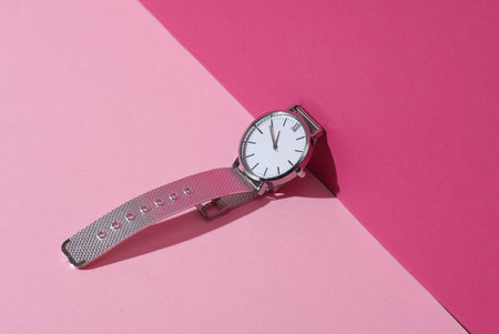 Women's analog silver wristwatch on pink pastel background with shadow. Creative layout. Minimalism