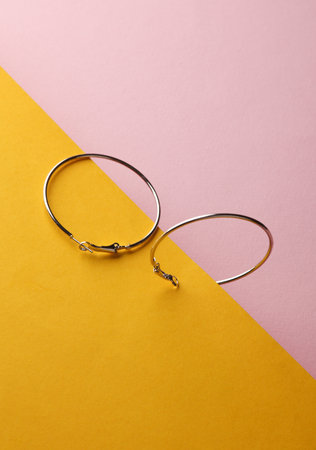 Silver hoop earrings on pink yellow background. Women's accessories, beauty concept. Creative layout, minimalismの写真素材