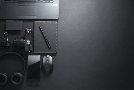 Modern black gadgets and accessories. Laptop, camera, smartphone, stereo headphones, notepad on a...