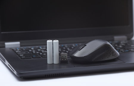 Wireless black pc mouse with batteries on laptop keyboard close-up