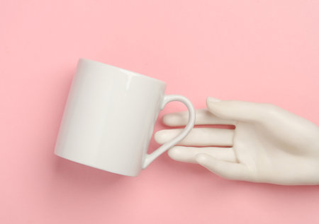 White mannequin hand holding ceramic cup on pink backgroundの写真素材