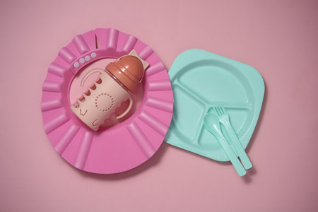 Set of plastic dishes for feeding baby, bib on a pink background. Top view. Flat layの写真素材