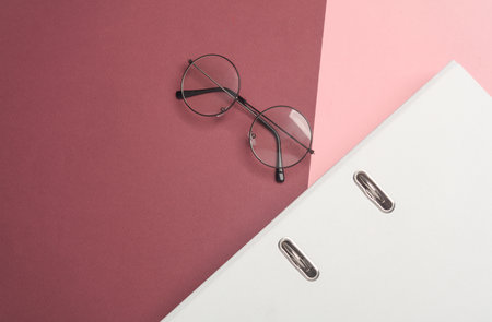 Stylish eyeglasses and folder on burgundy pink background. Flat lay. Top view. Business conceptの写真素材