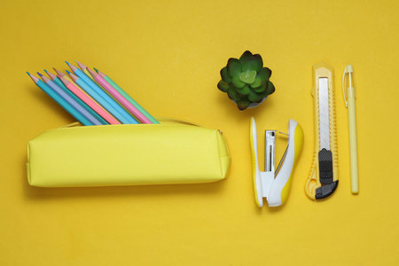 Yellow school pencil case with stationery and school accessories on a yellow background. Back to...