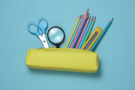 Yellow school pencil case with stationery and school accessories on a blue background. Back to school concept. Top view. Flat layの写真素材