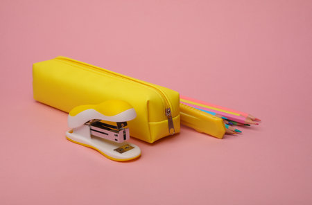 Yellow school pencil case with stationery and school accessories on pink background. Back to school...